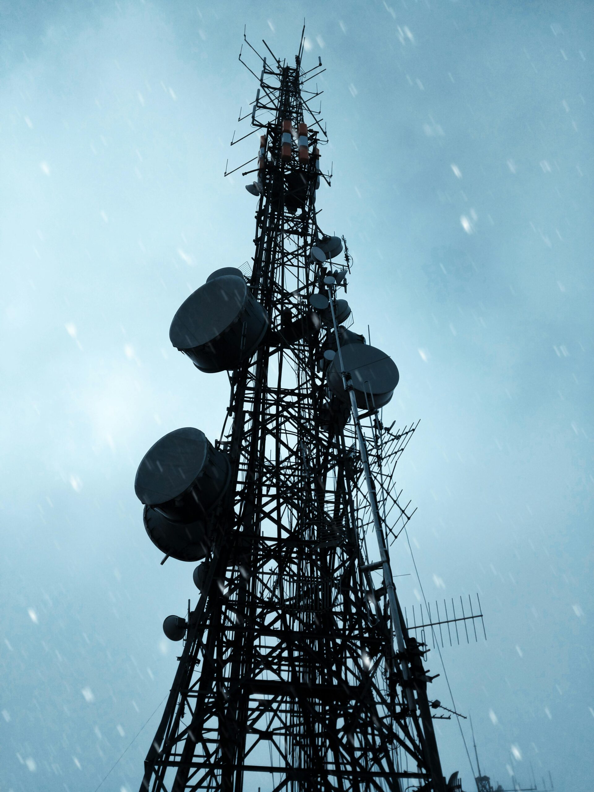 Low angle view of a telecommunication tower silhouetted against a dramatic, cloudy sky.