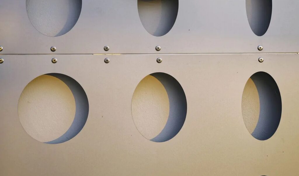 Wireless headphones hanging on a perforated geometric metal wall, showcasing modern design.
