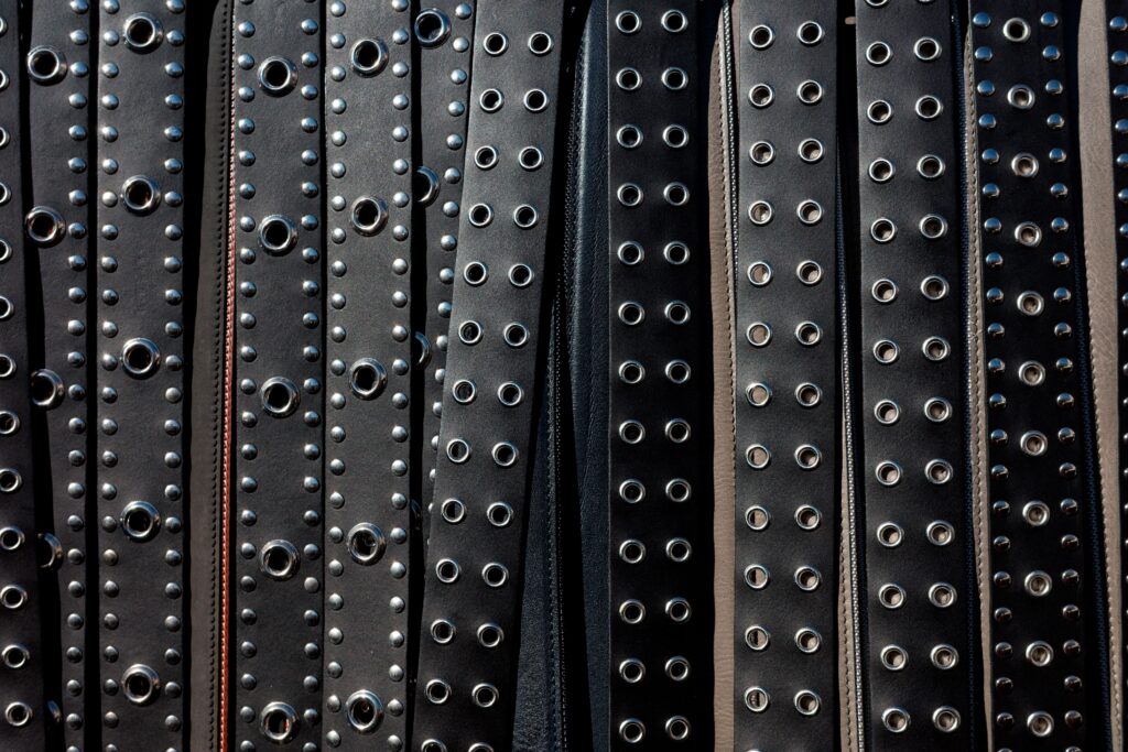 Close-up view of multiple black leather studded belts arranged in rows.