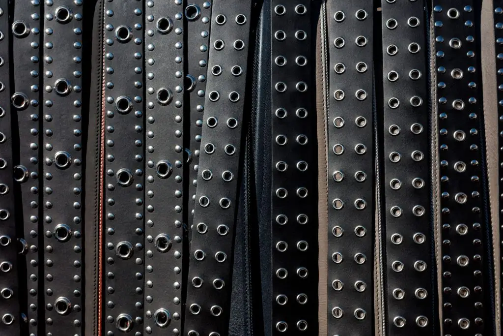Close-up view of multiple black leather studded belts arranged in rows.
